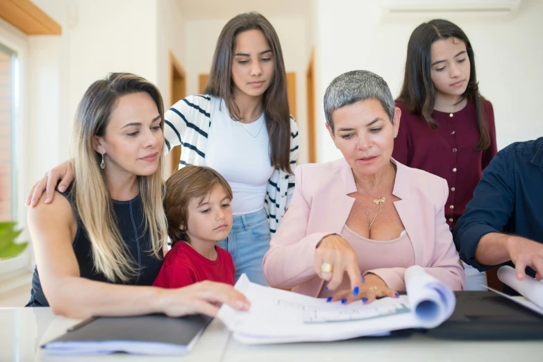 a group of people are gathered around a table, by Julian Allen, pexels contest winner, woman holding another woman, school curriculum expert, te pae, looking serious