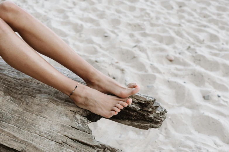 a woman sitting on a log on the beach, by Victorine Foot, trending on pexels, veins merged feet head, jewelry, standing on a shelf, manly
