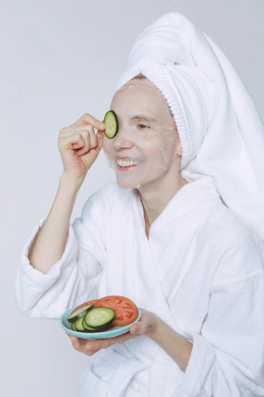 a woman with a towel on her head holding a plate with cucumbers on it, by Julia Pishtar, trending on pexels, silicone skin, old man doing with mask, on clear background, in robes