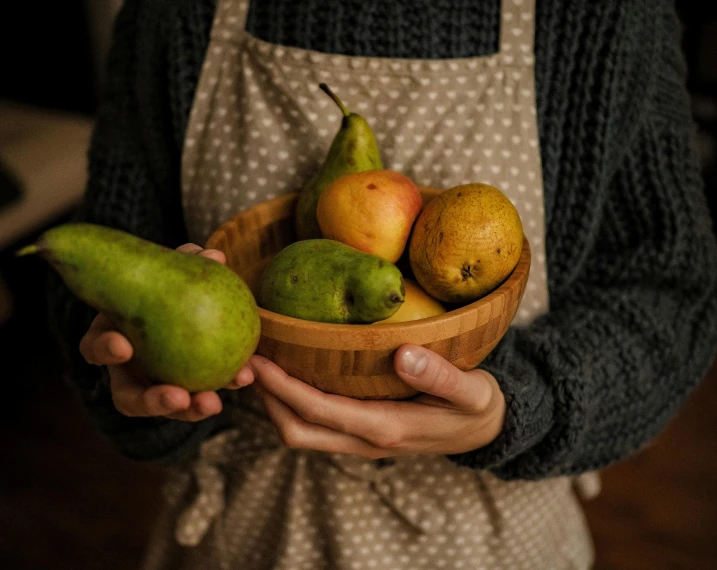 a woman in an apron holding a bowl of fruit, a still life, pexels contest winner, pears, sustainable materials, wearing a green sweater, presenting wares