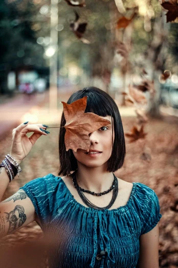a woman holding a leaf in front of her face, a portrait, pexels contest winner, with tattoos, square, mid fall, avatar image