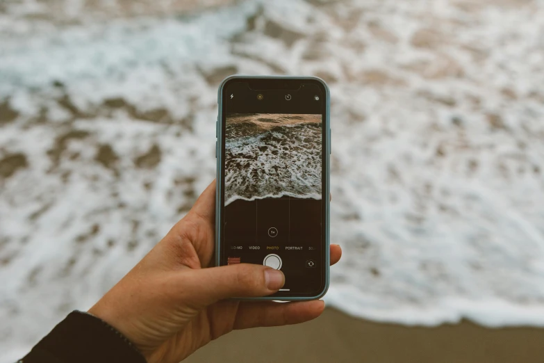 a person taking a picture of the ocean with their cell phone, a picture, by Niko Henrichon, unsplash contest winner, realism, ocean swells, holding it out to the camera, slightly pixelated, ground level shot