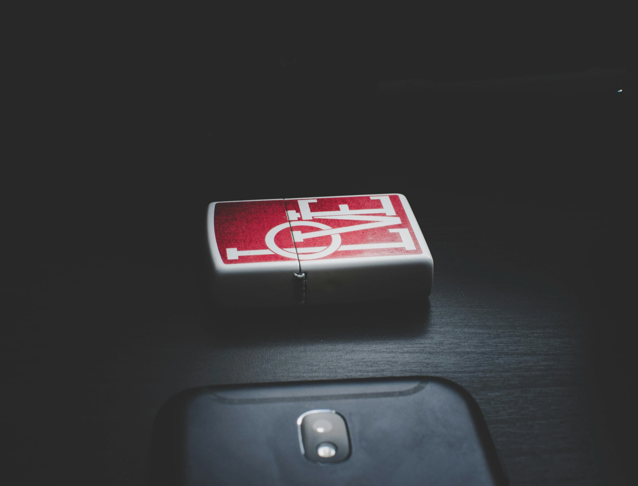 a cell phone sitting on top of a table, a picture, unsplash, postminimalism, playing card back, love hate love, red on black, concept art zippo lighter