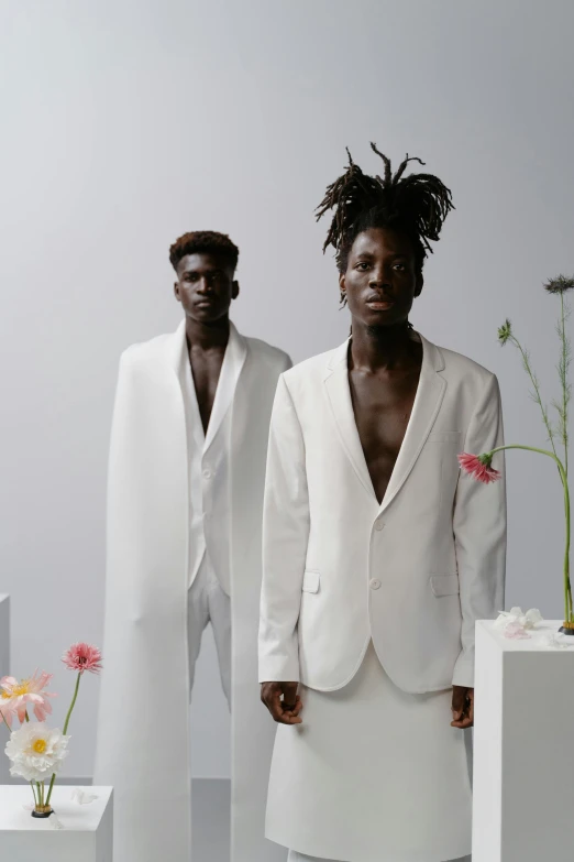 a couple of men standing next to each other, an album cover, inspired by Charles Martin, wearing white silk, adut akech, tall flowers, subject detail: wearing a suit