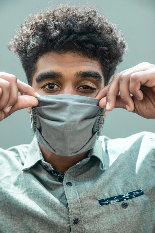 a man wearing a mask covering his face, by Alexander Brook, shutterstock, black teenage boy, dressed in a gray, surgeon, mischievous look