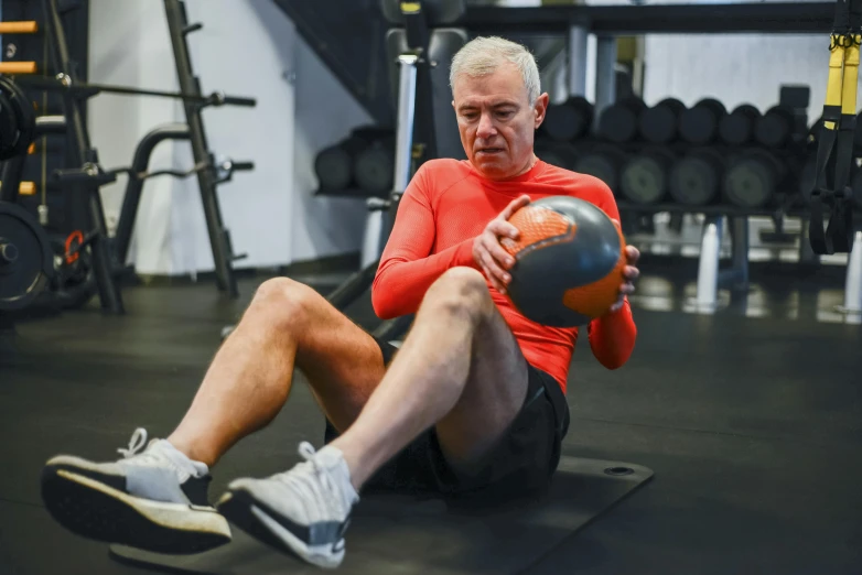 a man is sitting on a mat and holding a medicine ball