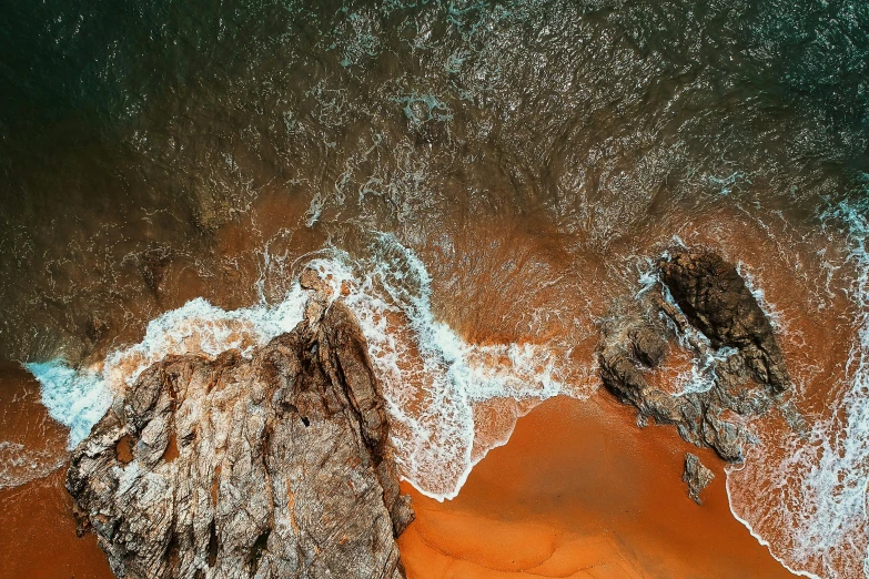 a couple of rocks sitting on top of a sandy beach, pexels contest winner, hd aerial photography, turbulent water, vibrant orange, wall of water either side