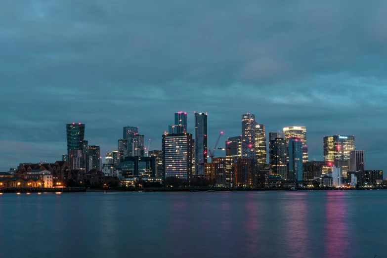 a large body of water with a city in the background, pexels contest winner, hyperrealism, canary wharf, blue hour lighting, grey, panoramic