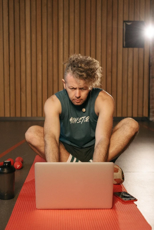 a man sitting on the floor with a laptop, by Julia Pishtar, dim dingy gym, james gleeson, mrbeast, still photograph