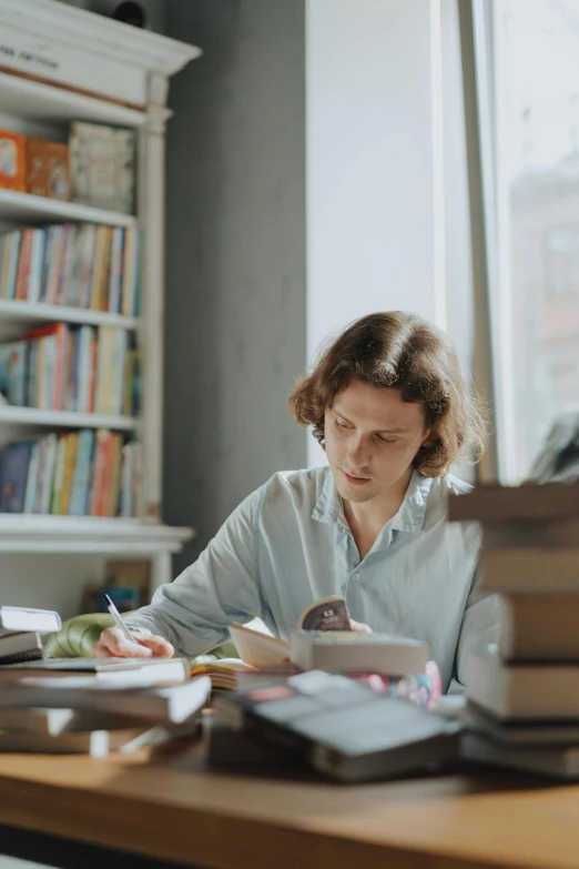 a woman sitting at a table in front of a pile of books, joe keery, working hard, ewa juszkiewicz, uncropped