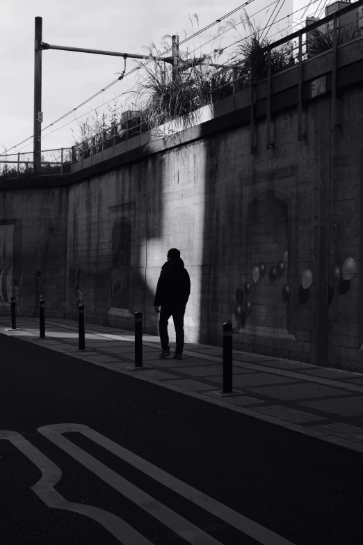 a black and white photo of a person walking down a street, a black and white photo, unsplash, conceptual art, wall darkness, in neotokyo, late morning, behind the wall