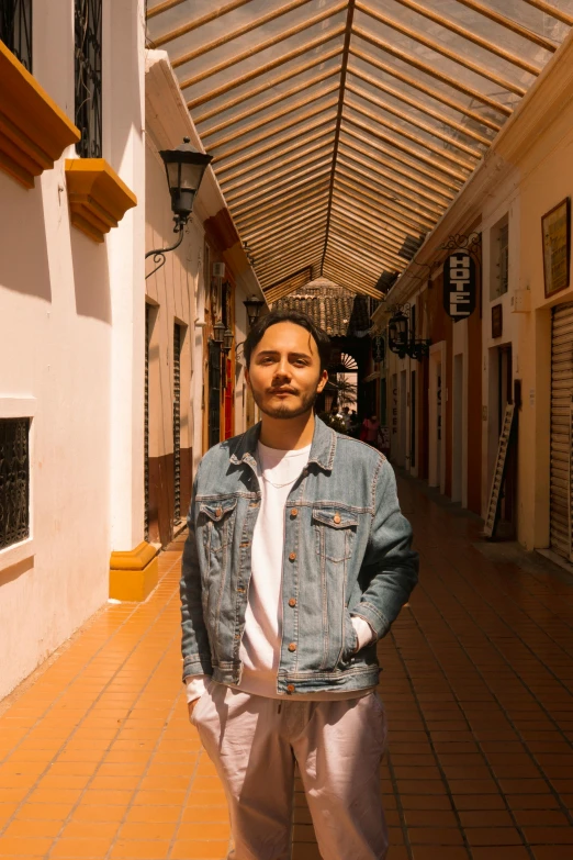 a man in jeans jacket and white tee - shirt walking down alley way