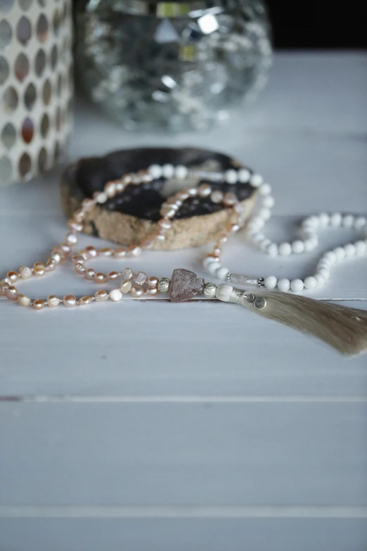 a close up of a necklace on a table, inspired by Perle Fine, unsplash, baroque, in a white boho style studio, linsey levendall, tassels, pearls of sweat