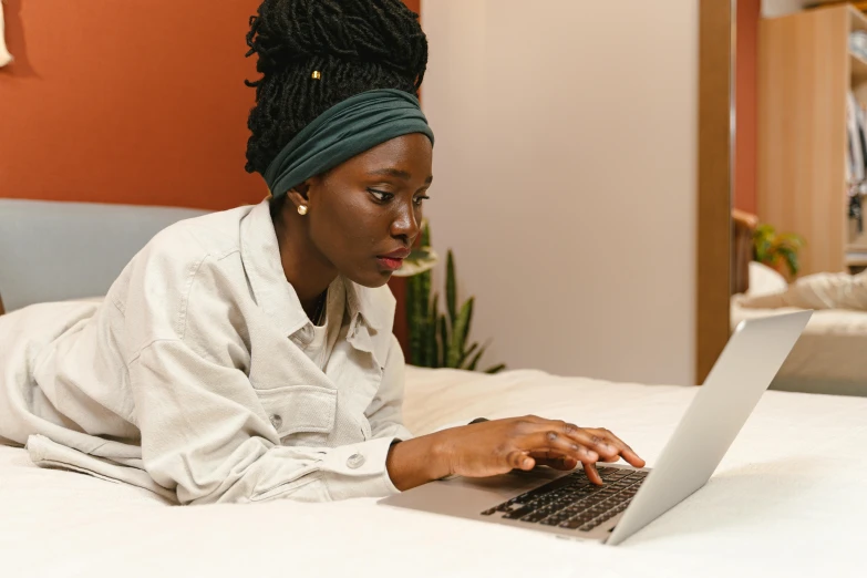 a woman laying on a bed using a laptop computer, trending on pexels, brown skin, avatar image, full profile, performing