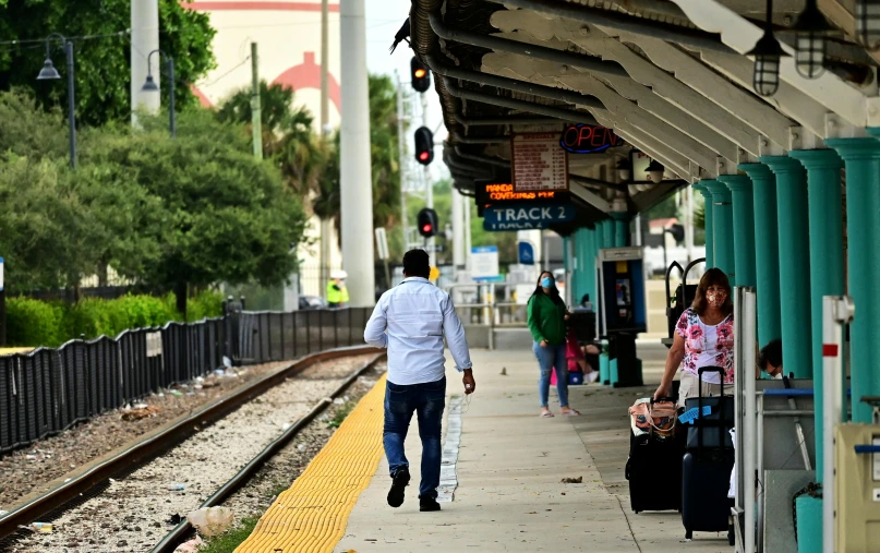 a group of people walking down a sidewalk next to a train station, florida man, not train tracks, ap news, a cozy