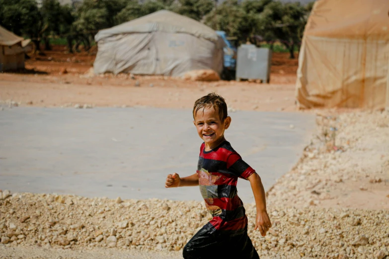 a young boy running with a frisbee in his hand, hurufiyya, makeshift houses, smiling and dancing, 2019 trending photo, real life photo of a syrian man