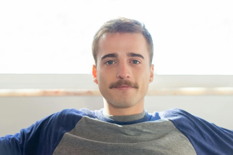 a man sitting on a couch in front of a window, a portrait, trending on reddit, with trimmed mustache, borja, medium head to shoulder shot, discord profile picture