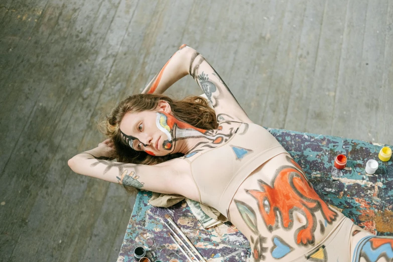 a woman laying on top of a skateboard covered in tattoos, inspired by Elsa Bleda, trending on pexels, hyperrealism, skintight rainbow body suit, alec soth : : love, inspired in balthus, angela sarafyan