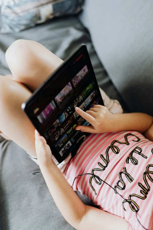 a little girl laying on a couch with a tablet, pexels, at netflix, dressed in a top and shorts, teenage, uncropped