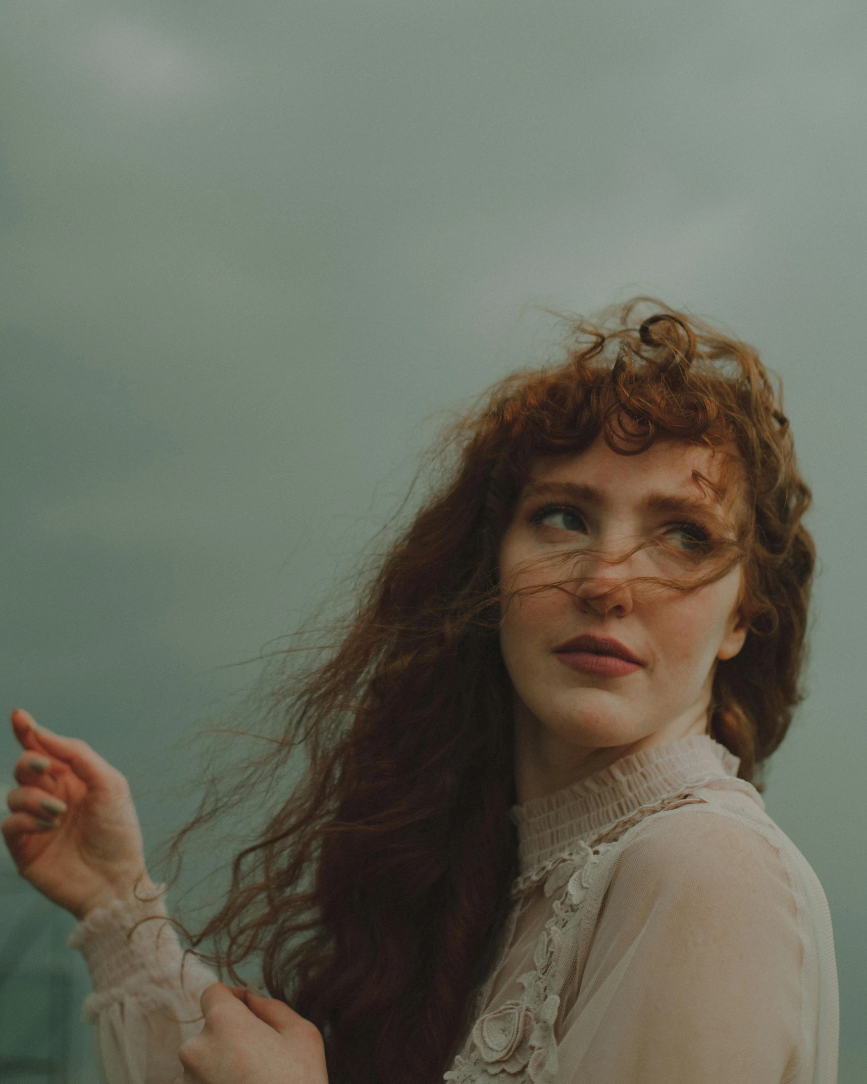 a woman with long red hair standing in front of a body of water, an album cover, inspired by Elsa Bleda, pexels contest winner, pre-raphaelitism, curly bangs, during a storm, still frame from a movie, a beautiful victorian woman