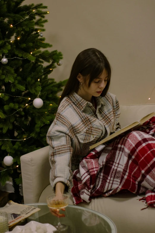 the woman is reading the magazine sitting next to the christmas tree