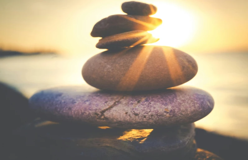 a stack of rocks sitting on top of a beach, unsplash, realism, sun flare, health spa and meditation center, instagram post, lights on