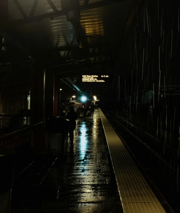 a train station with rain on the platform and people walking