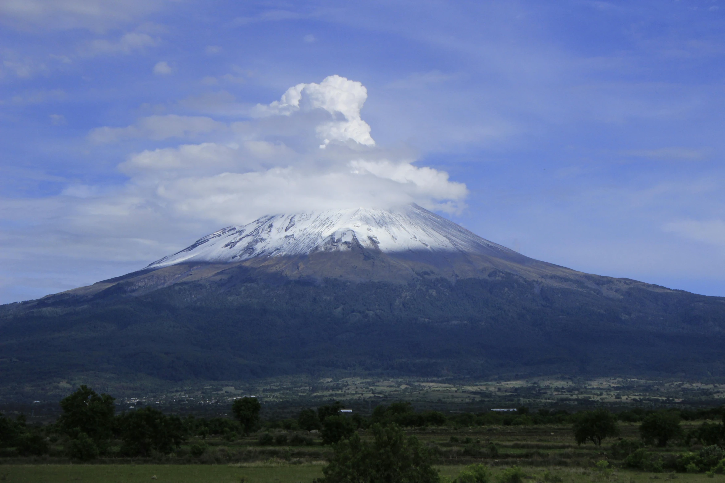 a mountain covered in snow, surrounded by trees and clouds