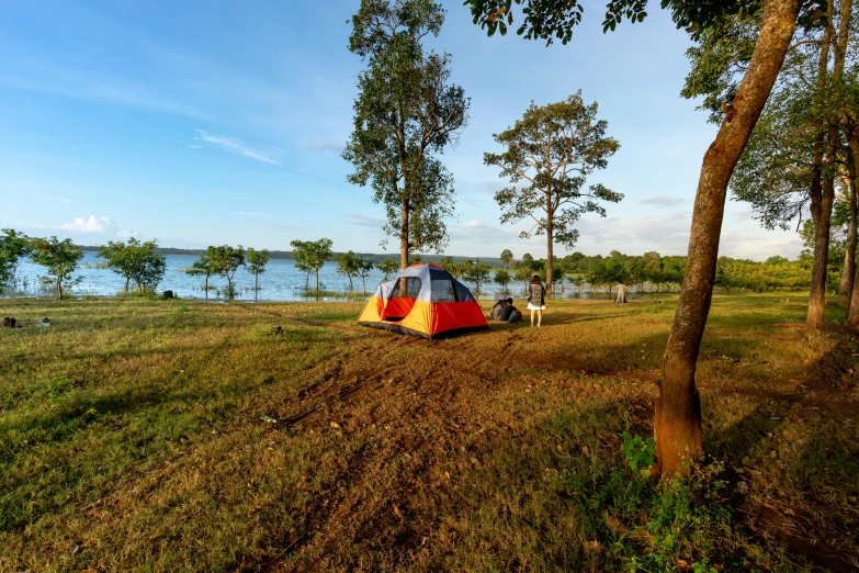 a red and yellow tent sitting on top of a lush green field, hurufiyya, lake view, cambodia, camping, slide show