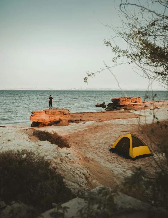 a yellow tent sitting on top of a sandy beach, unsplash contest winner, standing on rock, fishing, split near the left, he is at camp