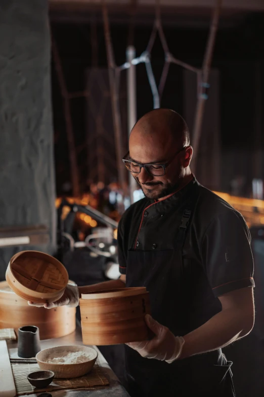 a man standing in a kitchen preparing food, inspired by Kanō Naizen, process art, on a dark background, vessels, precision, chilean