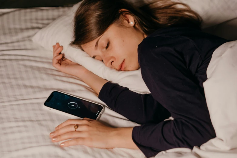 a woman laying on top of a bed next to a cell phone, trending on pexels, portrait of a woman sleeping, slightly turned to the right, 1 5 0 4, heart rate