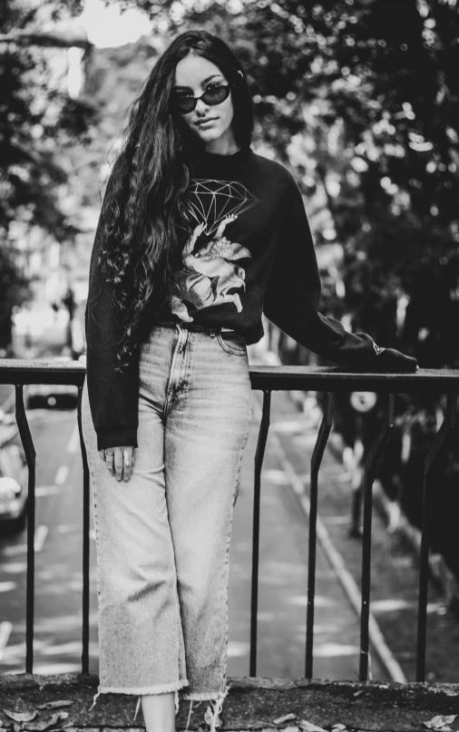 a black and white photo of a woman leaning on a fence, a black and white photo, by Tamas Galambos, pexels contest winner, realism, kawaii shirt and jeans, wearing sweatshirt, 15081959 21121991 01012000 4k, female with long black hair