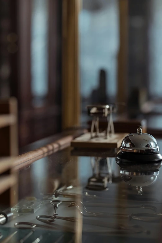 a silver bell sitting on top of a glass counter, a tilt shift photo, by Daniel Seghers, renaissance, the grand budapest hotel, pair of keycards on table, fine details 8k octane rendering, promo image