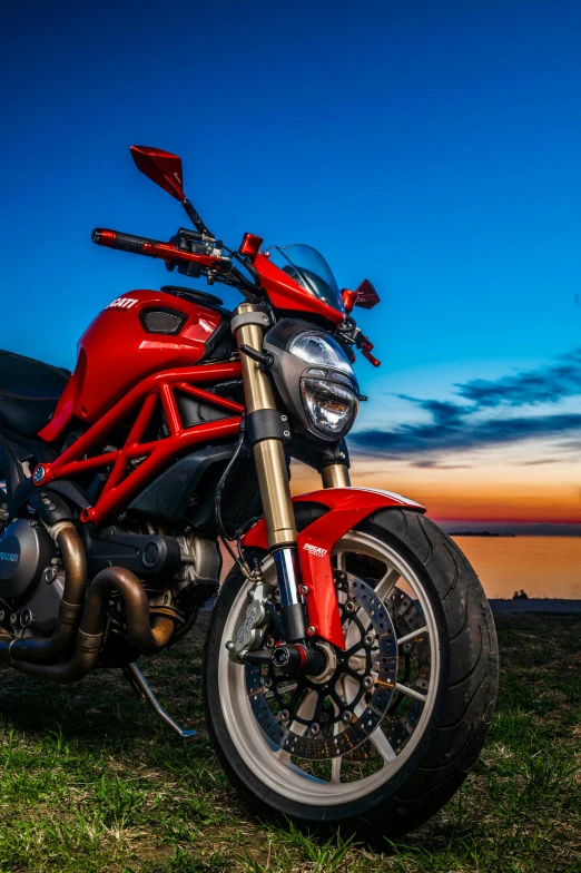 a red motorcycle parked on top of a lush green field, during a sunset, profile image, blue, devil's horns
