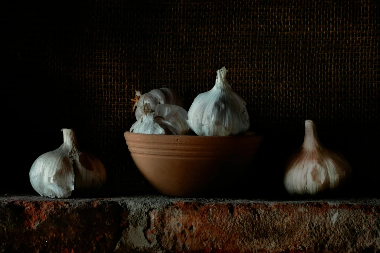 a bowl of garlic next to three heads of garlic, a still life, unsplash, renaissance, terracotta, low lighting, in a kitchen, lpoty