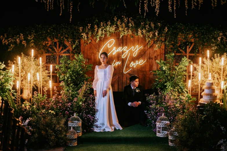 a woman in white standing on grass next to an archway with lit candles