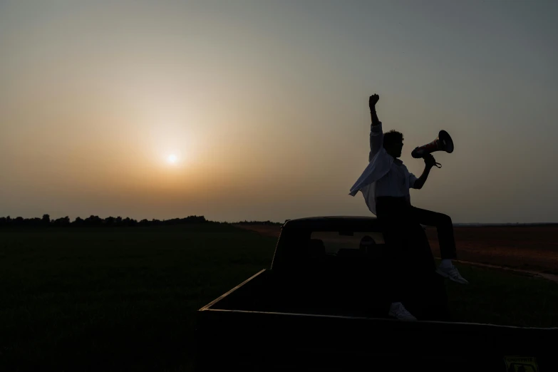 a man sitting on top of a truck holding a baseball bat, an album cover, by Eglon van der Neer, pexels contest winner, happening, silhouettes in field behind, arms raised, early evening, press shot