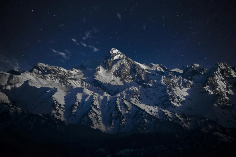 the stars illuminate the snow - capped mountains at night