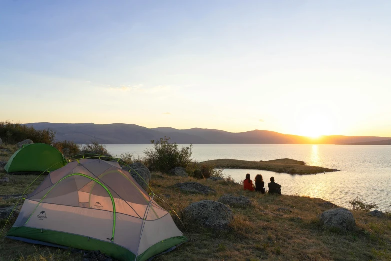 a couple of tents sitting next to a body of water, by Muggur, sunset lighting, high elevation, family friendly, ayne haag