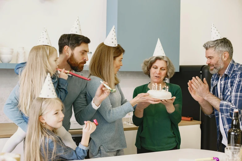 a group of people standing around a table with a cake, wearing a party hat, profile image