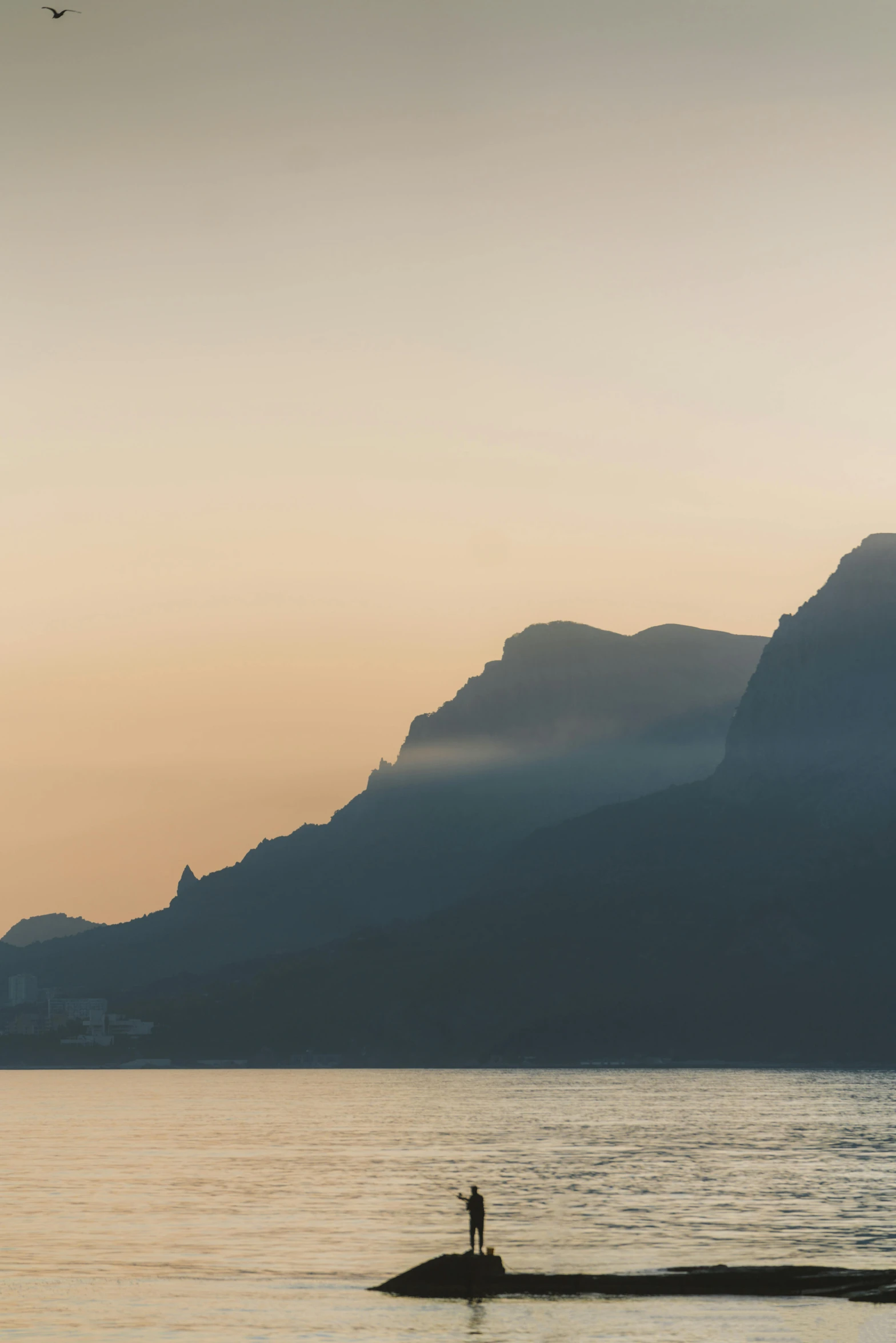 a man standing on top of a beach next to a body of water, by Daniel Seghers, trending on unsplash, romanticism, sun rises between two mountains, alvaro siza, photo taken from a boat, monaco