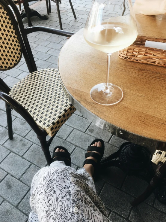 a person sitting at a table with a glass of wine, a picture, birkenstock sandals, cafe, instagram story, profile image