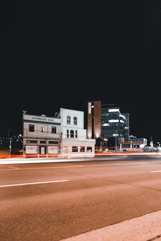 a red fire hydrant sitting on the side of a road, a black and white photo, by Andrew Stevovich, unsplash contest winner, night life buildings, long exposure outside the city, white building, intersection