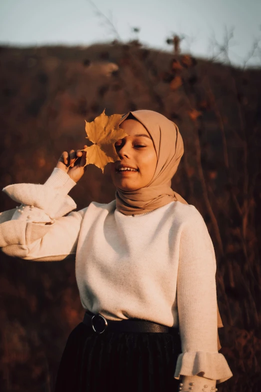 a woman holding a leaf up to her face, pexels contest winner, hurufiyya, wearing casual clothes, muslim, 🍂 cute, light tan