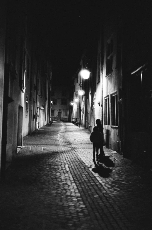 a black and white photo of a person walking down a street at night, streets of heidelberg, shes alone, instagram picture, light over boy