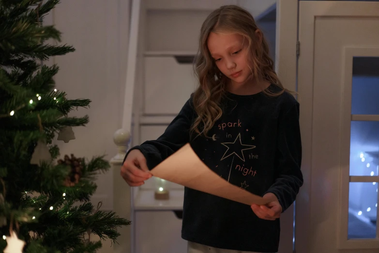 a girl opening a gift under a christmas tree