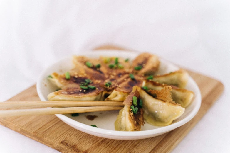 a close up of a plate of food with chopsticks, dumplings on a plate, with a white background, on a wooden plate, ❤🔥🍄🌪