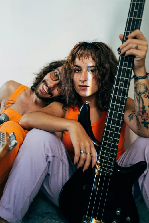 a man sitting next to a woman holding a guitar, an album cover, trending on pexels, antipodeans, purple mullet, tilt and orange, sweaty, bassist