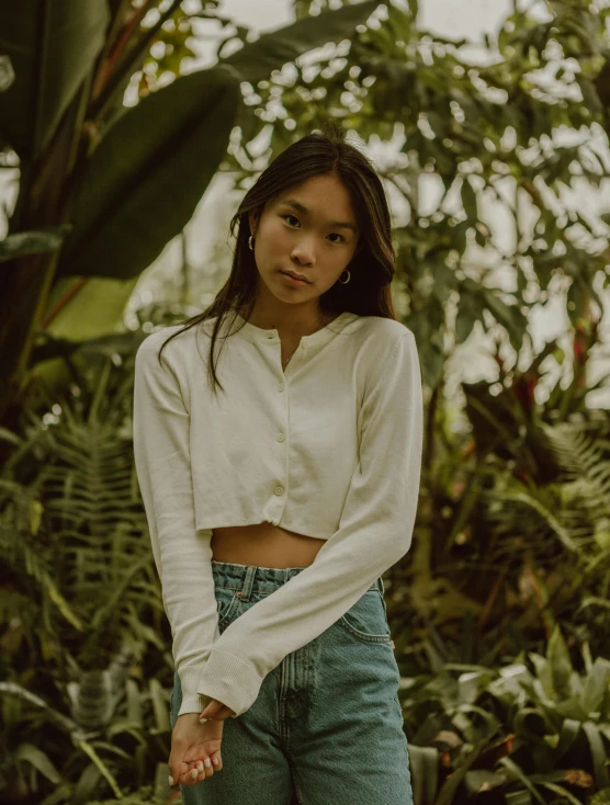 a woman standing in front of a lush green forest, an album cover, by Robbie Trevino, unsplash contest winner, wearing a white button up shirt, wearing a crop top, wearing in cardigan, young asian girl